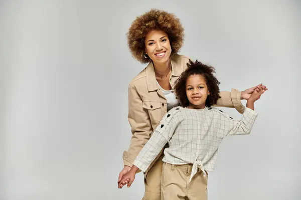 stock image A curly African American mother and daughter, in stylish clothing, striking a pose on a grey background.