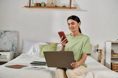 Dizüstü bilgisayarda çalışırken yatakta oturan sıradan giyinmiş bir kadın..