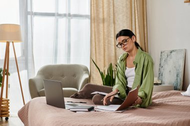 Gündelik giyinmiş bir kadın yatağında dizüstü bilgisayarda çalışıyor..
