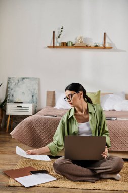 Sıradan giyinmiş bir kadın, yerde otururken dizüstü bilgisayar kullanıyor..