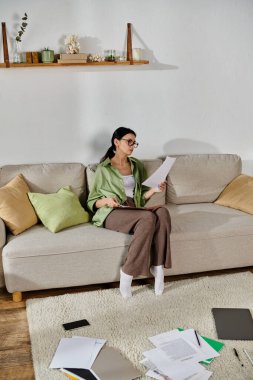 Woman in casual attire reading paper on a couch. clipart