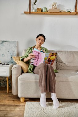 Kanepede günlük giyinmiş bir kadın dergisi okuyor..