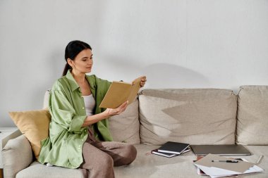 Sıradan giyinmiş bir kadın kanepeye oturur ve mutlu bir şekilde kitap okur..