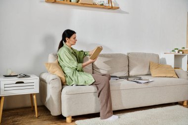 Kanepede dinlenirken kitaba dalmış bir kadın..