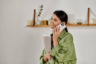 Gündelik kıyafetli bir kadın, elinde telefon ve kağıtlarla birden fazla iş yapıyor..