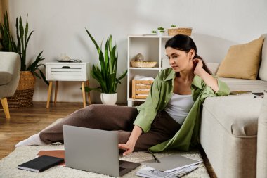 Gündelik giysiler içinde şık bir kadın yerde oturuyor, dizüstü bilgisayara odaklanmış..