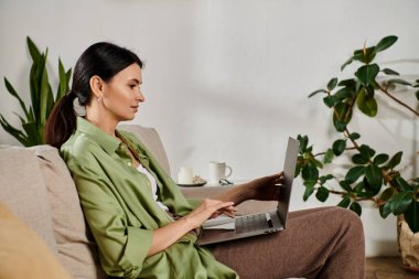 Modern bir kanepenin rahatlığıyla, şık bir kadın laptopunda birden fazla iş yapıyor..