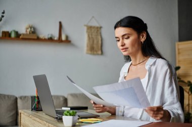 A woman in casual attire is seated at a desk surrounded by papers. clipart