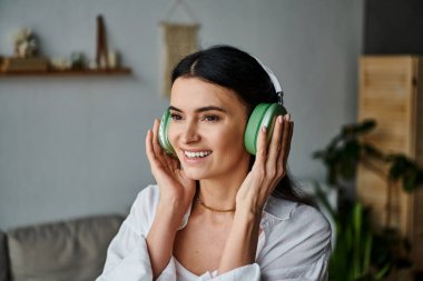 Sıradan giyinmiş bir kadın evde dinlenirken kulaklıkla müzik dinliyor..