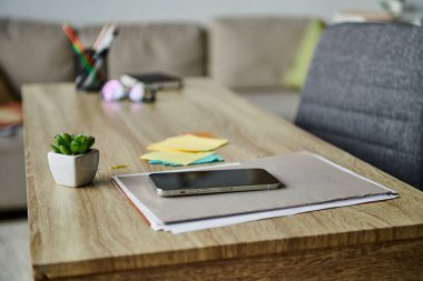 Wooden table with cell phone next to potted plant. clipart