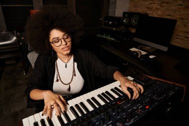 A woman wearing glasses plays a keyboard in a recording studio during a music band rehearsal. clipart