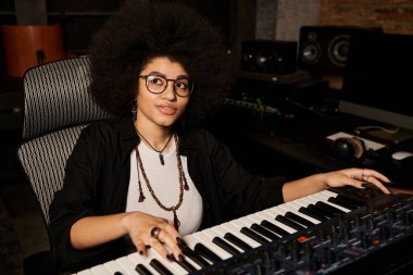 A talented woman in glasses plays a keyboard with passion and focus in a recording studio during a music band rehearsal. clipart
