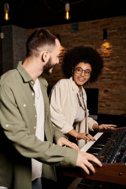 A man and woman stand beside a keyboard in a recording studio, immersed in creating music for their band rehearsal. clipart