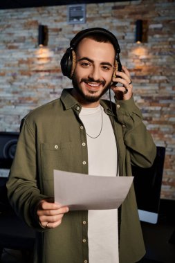 Bandoyla provadan önce kayıt stüdyosunda müzik notaları tutan kulaklıklı bir müzisyen..