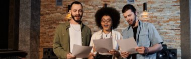 A music band rehearses, holding papers in front of a brick wall in a recording studio. clipart