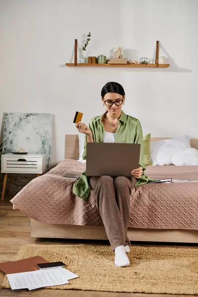 stock image Woman in casual attire using laptop and credit card on bed.