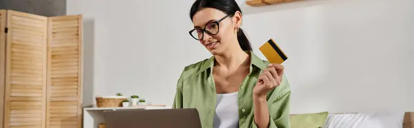 stock image A woman multitasking with a credit card and laptop.