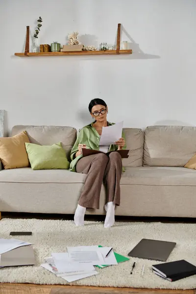 stock image A woman immersed in papers while seated on a cozy couch.