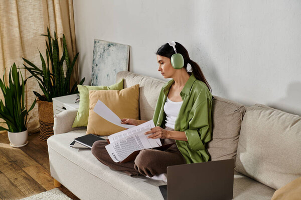 A woman in casual attire sitting on a couch engrossed in paperwork.