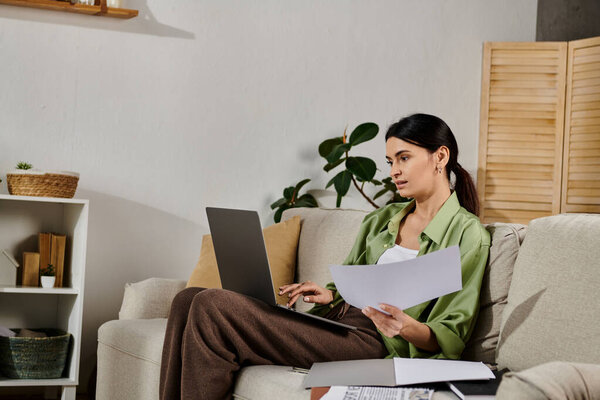 Woman working on laptop while seated on couch.