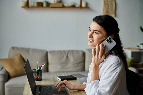 A woman multitasking with a phone call and laptop work.