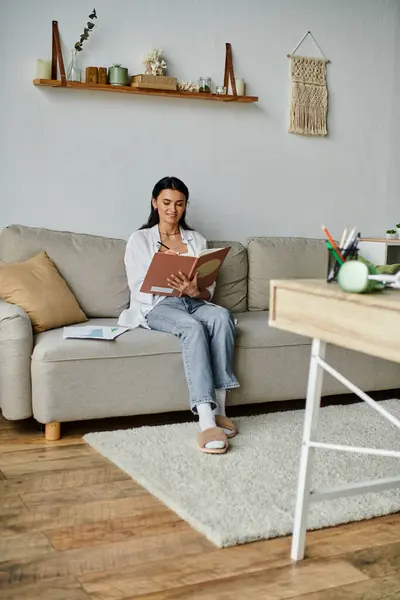 stock image A woman engrossed in a book on a cozy couch.