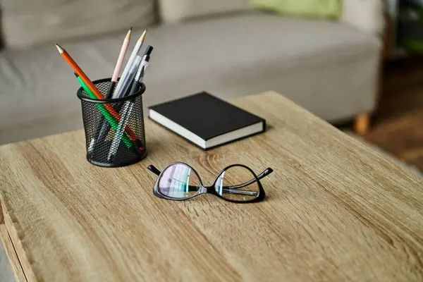 stock image A wooden table with a cup of pencils and a pair of glasses.