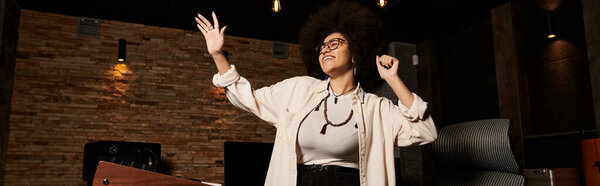 Женщина радостно поднимает руки в студии звукозаписи во время репетиции музыкальной группы.