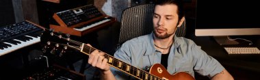 Müzik grubu provası sırasında bir müzik stüdyosunda bilgisayarın önünde gitar çalan bir adam..