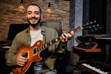 Müzik grubunun provasında gitar tıngırdatan bir adam neşeyle gülümsüyor..