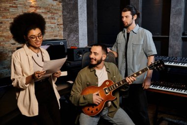 Bir müzik grubu, akustik gitar çalmaya odaklanmış bir grup insanla bir kayıt stüdyosunda prova yapıyor..