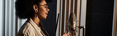 A talented woman passionately sings into a microphone during a music band rehearsal in a recording studio. clipart