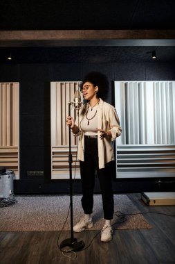 Bir kadın, bir müzik grubu provası sırasında mikrofona şarkı söylemeye hazır bir şekilde kayıt stüdyosunda güvenle duruyor..