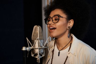 A woman with glasses passionately sings into a microphone during a music band rehearsal in a recording studio. clipart