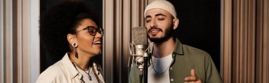Bir adam ve bir kadın, bir müzik grubu provasında mikrofona tutkulu bir şekilde şarkı söylüyorlar..