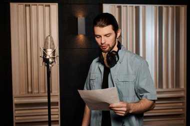 A man in a recording studio studying a sheet of paper during a music band rehearsal. clipart