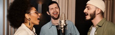 Bir müzik grubu, ses ekipmanları ve mikrofonlarla çevriliyken uyum içinde şarkı söyleyerek bir kayıt stüdyosunda prova yapıyor..