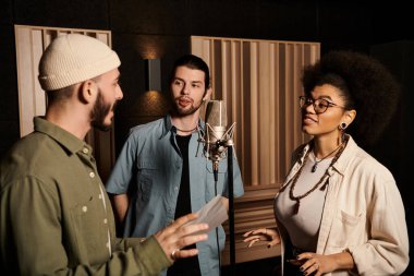 Three individuals converse animatedly in a recording studio, preparing for a music band rehearsal. clipart