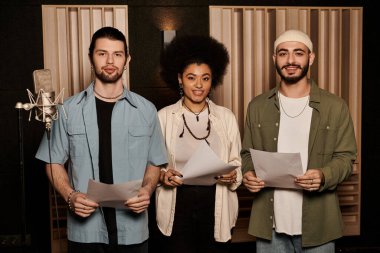 Three individuals stand in a recording studio holding lyric sheets, preparing for a music band rehearsal session. clipart