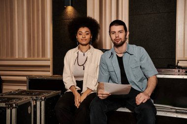 Bir erkek ve kadın müzik aletleri ve ekipmanlarıyla çevrili bir kayıt stüdyosunda iş birliği yapıyorlar..