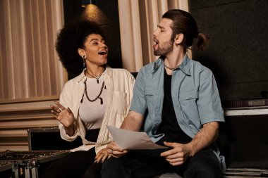 Bir erkek ve kadın müzik stüdyosunda müzik aletleri ve ekipmanlarla çevrili bir şekilde iş birliği yapıyorlar..
