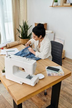 Masada oturan genç bir kadın, kıyafetlerini dikmek için dikiş makinesi kullanıyor..