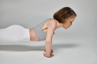 Attractive woman in comfy attire energetically doing push ups on white background. clipart