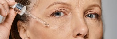 Rahat giyinmiş olgun bir kadın yüzüne serum sürüyor.