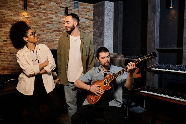 Разнообразная группа людей сотрудничает в студии звукозаписи с одним человеком, играющим на гитаре.