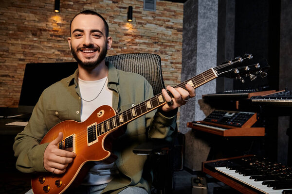 A man joyfully smiles while strumming a guitar in a music band rehearsal at a recording studio.