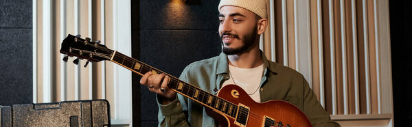 A man in a hat passionately plays an electric guitar during a music band rehearsal in a recording studio.