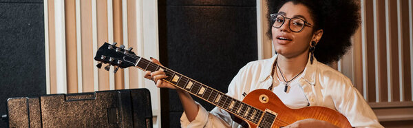 Талантливая женщина в очках страстно играет на электрогитаре во время репетиции музыкальной группы в студии звукозаписи.