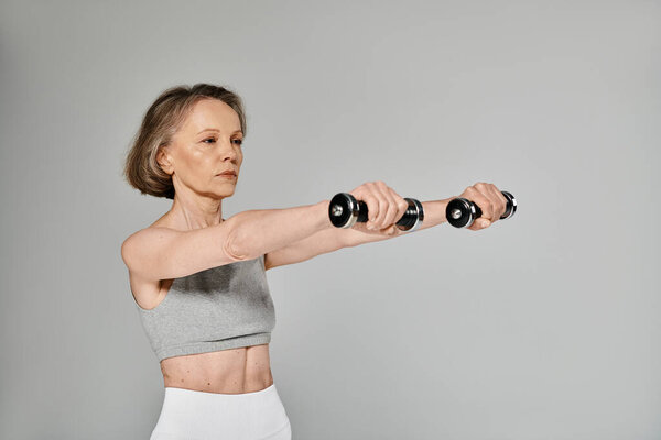 Elderly lady doing dumbbell exercises on gray background.