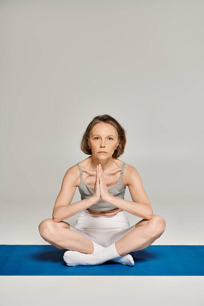 Зрелая, привлекательная женщина в удобной одежде изящно практикует йогу на мирном синем фоне.